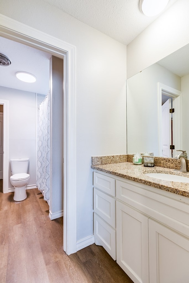 full bath with a textured ceiling, toilet, wood finished floors, vanity, and baseboards