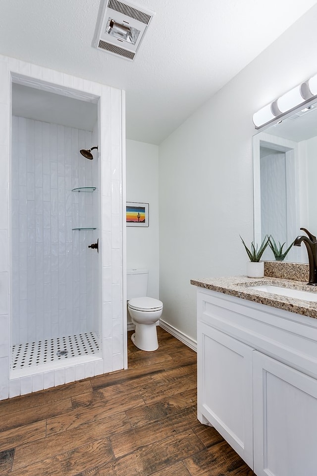 bathroom with toilet, wood finished floors, vanity, visible vents, and tiled shower