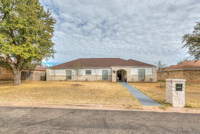 ranch-style home with stone siding, fence, and a front lawn