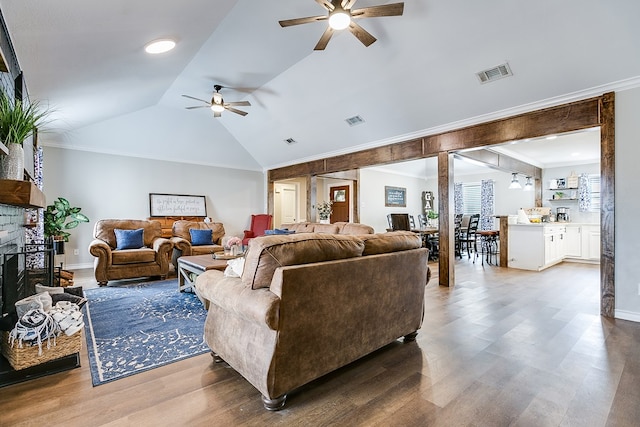 living area featuring a fireplace with raised hearth, wood finished floors, visible vents, vaulted ceiling, and ornamental molding