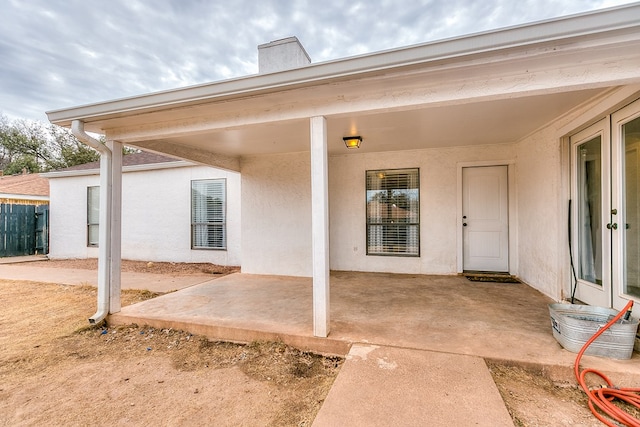 view of exterior entry with stucco siding, fence, and a patio