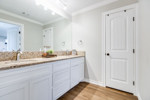 bathroom with double vanity, visible vents, ornamental molding, a sink, and wood finished floors