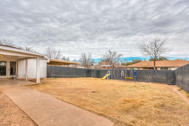 view of yard with a fenced backyard, a playground, and french doors