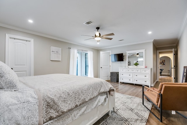 bedroom featuring ornamental molding, arched walkways, visible vents, and wood finished floors