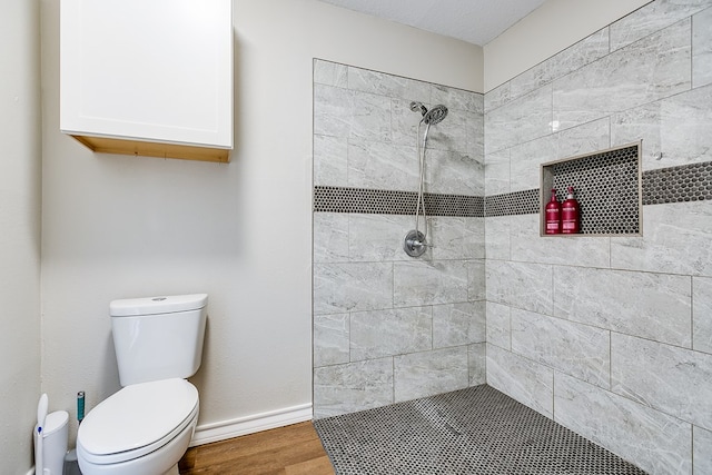 bathroom with toilet, baseboards, a tile shower, and wood finished floors