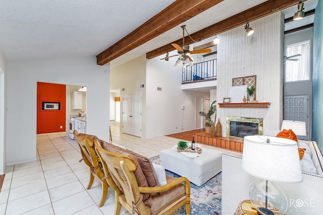 living room with light tile patterned floors, ceiling fan, vaulted ceiling with beams, a textured ceiling, and a brick fireplace