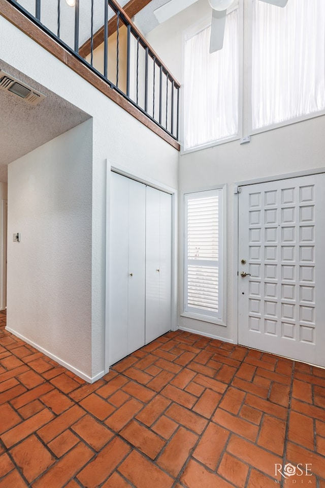 foyer entrance with a towering ceiling, a textured ceiling, and ceiling fan