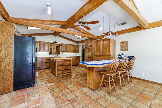 kitchen featuring a kitchen island, black refrigerator, tasteful backsplash, a kitchen bar, and ceiling fan