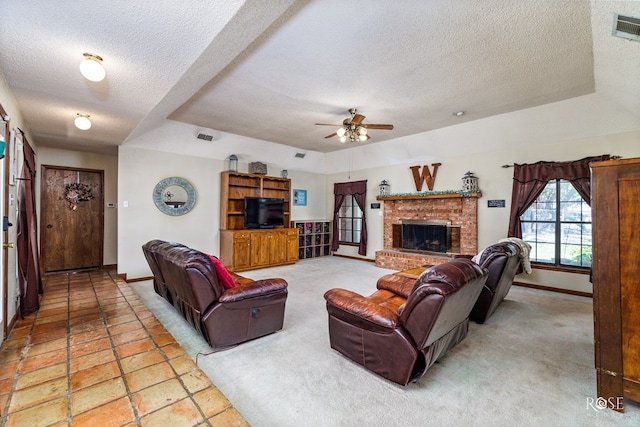 living room with ceiling fan, a tray ceiling, a brick fireplace, and a textured ceiling