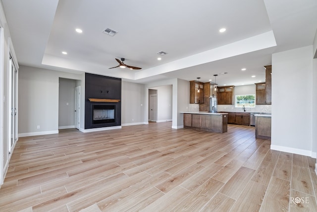 unfurnished living room with ceiling fan, a fireplace, a tray ceiling, and sink