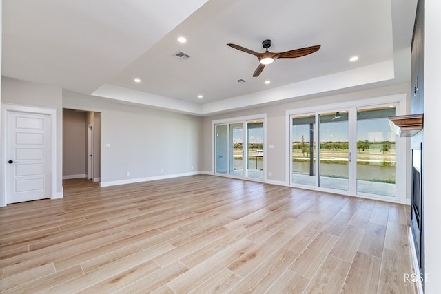 unfurnished room with light wood-type flooring, ceiling fan, and a tray ceiling