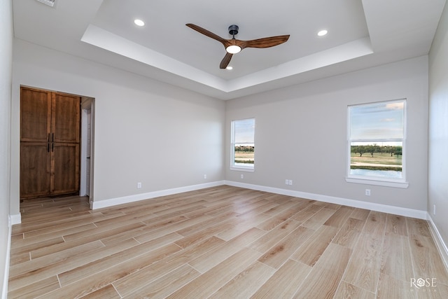 spare room with a raised ceiling, ceiling fan, and light wood-type flooring