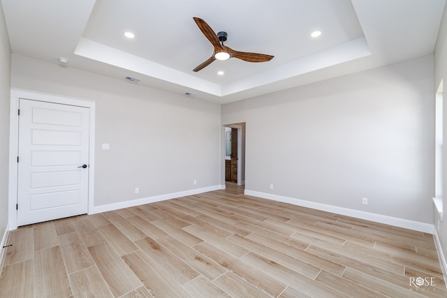 unfurnished room featuring a tray ceiling, ceiling fan, and light wood-type flooring