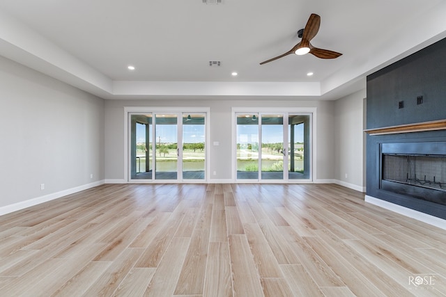 unfurnished living room with a raised ceiling, ceiling fan, and light wood-type flooring