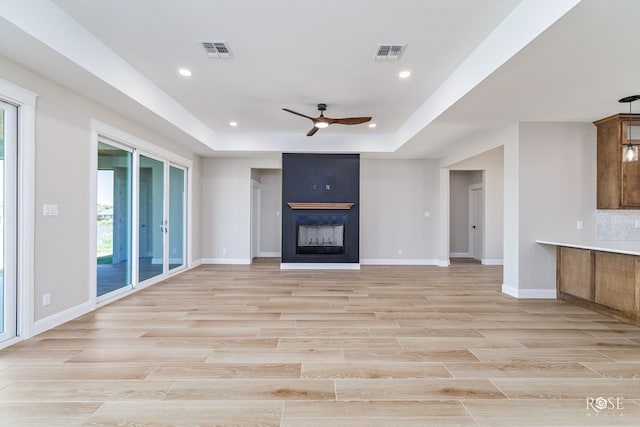 unfurnished living room featuring a raised ceiling, ceiling fan, and a fireplace