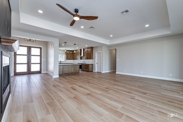 unfurnished living room featuring french doors, ceiling fan, a tray ceiling, and light hardwood / wood-style floors