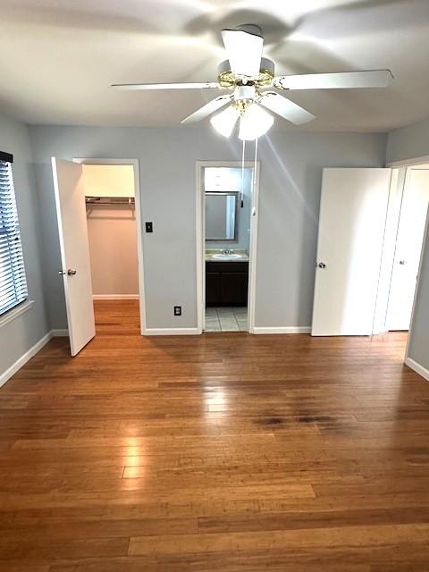 unfurnished bedroom featuring sink, ensuite bath, a spacious closet, ceiling fan, and light hardwood / wood-style floors