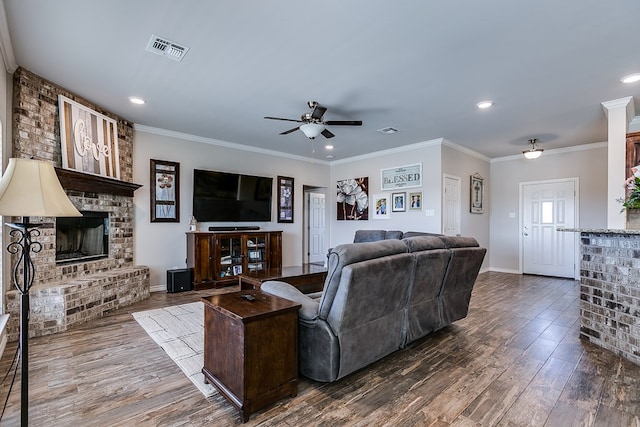 living room featuring crown molding, ceiling fan, dark hardwood / wood-style floors, and a brick fireplace