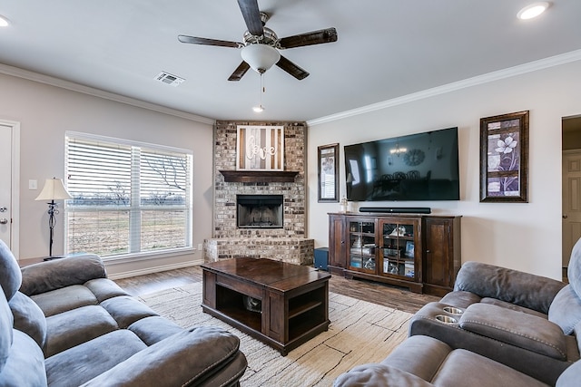 living room with crown molding, a brick fireplace, ceiling fan, and light hardwood / wood-style floors