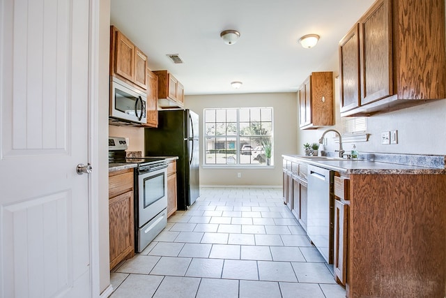 2902 Freeland St, San Angelo, TX 76901 - kitchen with appliances with stainless steel finishes, a sink, brown cabinets, light tile patterned floors, and baseboards