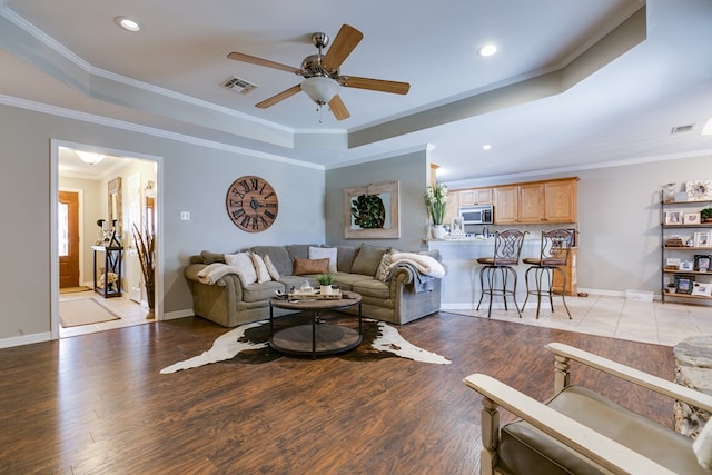 living room with crown molding, light wood-type flooring, ceiling fan, and a tray ceiling