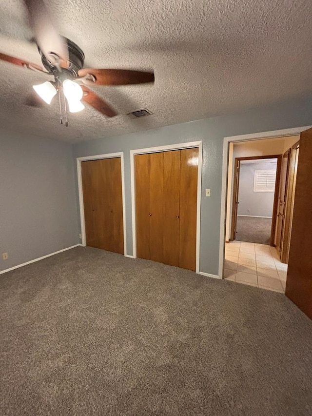 unfurnished bedroom featuring ceiling fan, two closets, light colored carpet, and a textured ceiling