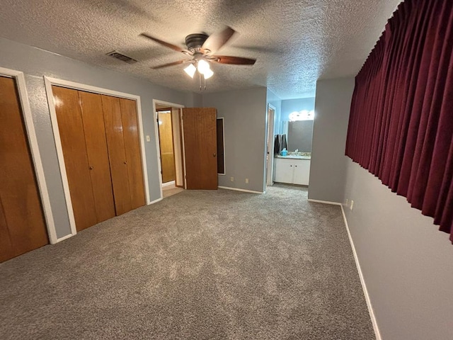 unfurnished bedroom featuring multiple closets, ensuite bath, carpet flooring, and a textured ceiling