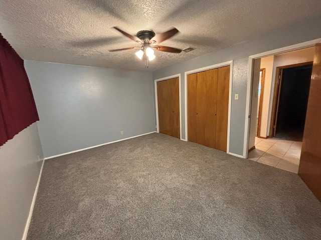 unfurnished bedroom featuring multiple closets, ceiling fan, light colored carpet, and a textured ceiling