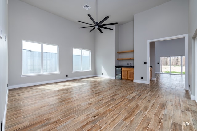 unfurnished living room with ceiling fan, bar, beverage cooler, and high vaulted ceiling