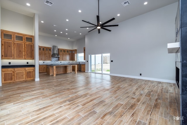 unfurnished living room featuring ceiling fan, a tiled fireplace, sink, and a high ceiling