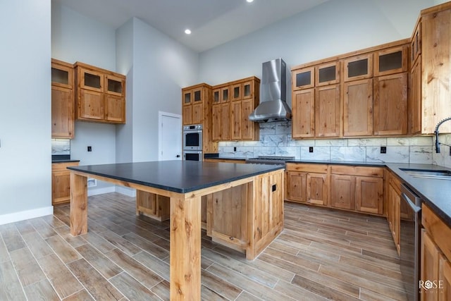 kitchen with wall chimney range hood, sink, light hardwood / wood-style flooring, appliances with stainless steel finishes, and a high ceiling