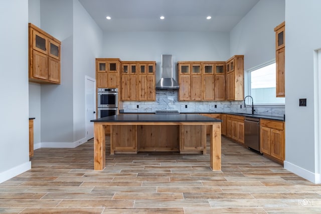 kitchen featuring wall chimney range hood, sink, stainless steel appliances, a center island, and a kitchen bar