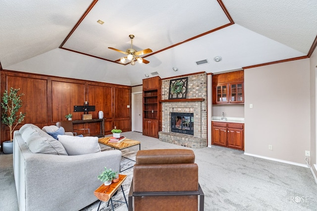 carpeted living room with ceiling fan, ornamental molding, a fireplace, and vaulted ceiling