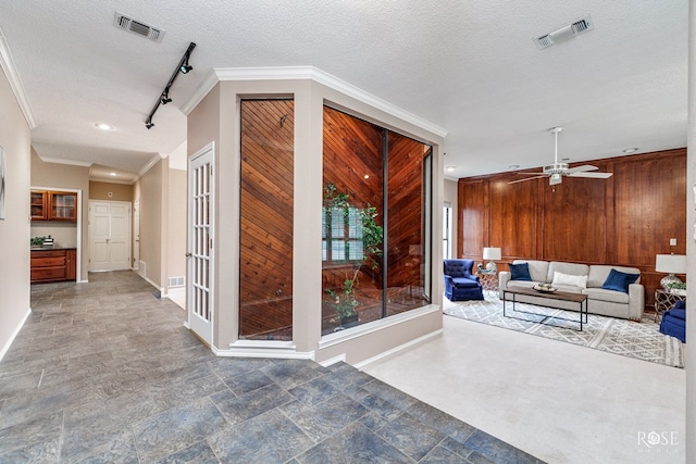corridor with crown molding, track lighting, wooden walls, and a textured ceiling