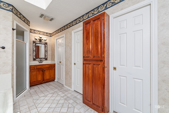 bathroom with vanity, a skylight, a textured ceiling, and walk in shower