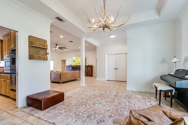 tiled living room with a tray ceiling, ceiling fan with notable chandelier, ornamental molding, and ornate columns