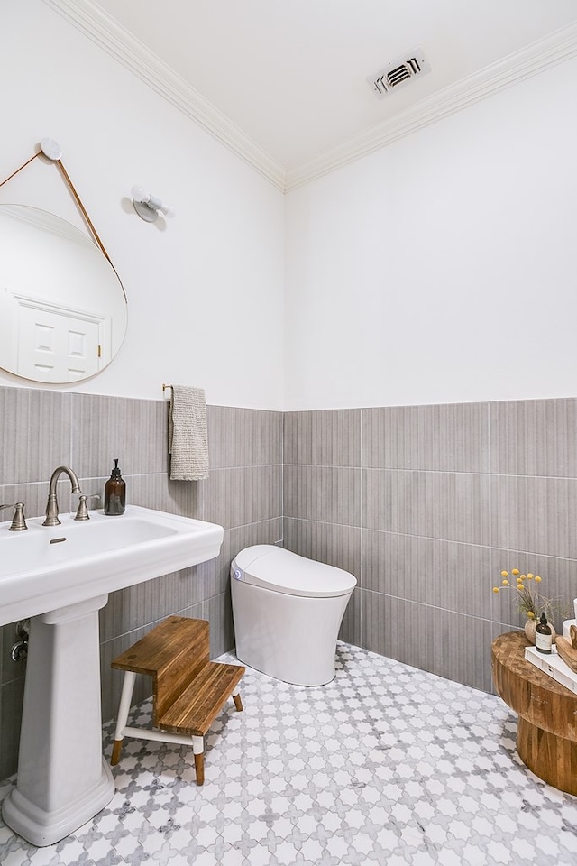 bathroom featuring ornamental molding, toilet, sink, and tile walls