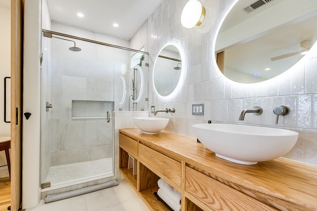 bathroom with ceiling fan, tile walls, vanity, a shower with shower door, and tile patterned floors