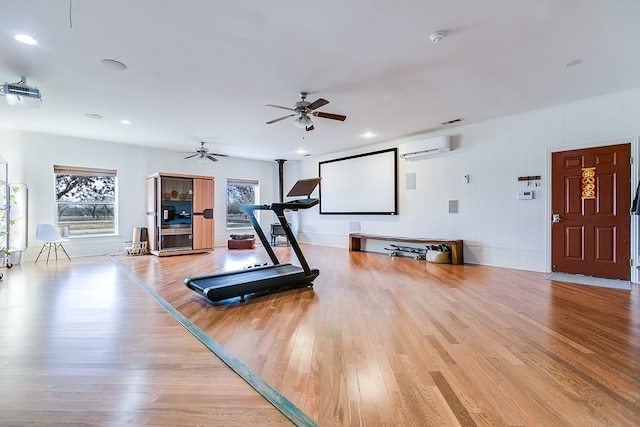 exercise area featuring ceiling fan, an AC wall unit, and light wood-type flooring