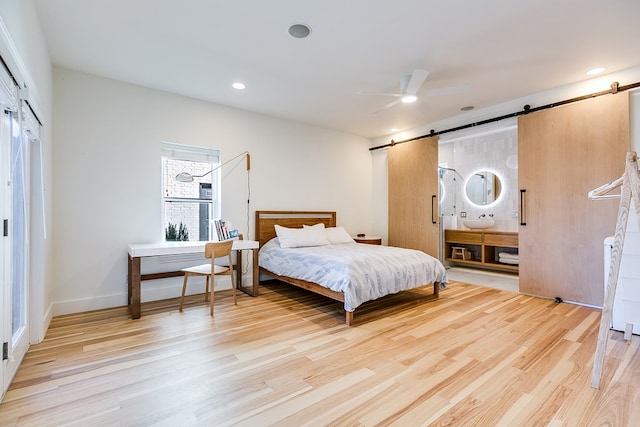 bedroom featuring sink, ceiling fan, light hardwood / wood-style floors, a barn door, and a closet