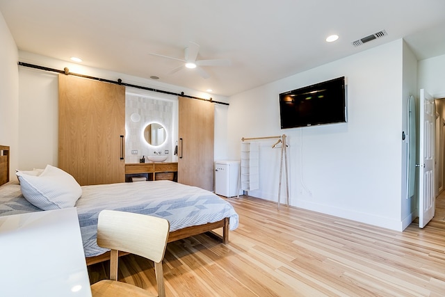 bedroom featuring ceiling fan, a barn door, and light hardwood / wood-style flooring