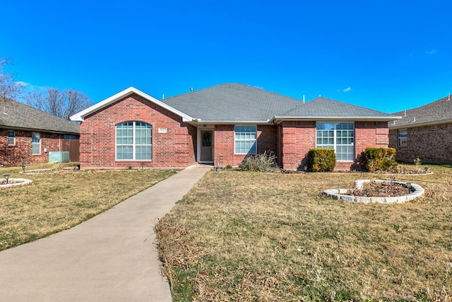 ranch-style house featuring a shingled roof, a front yard, and brick siding