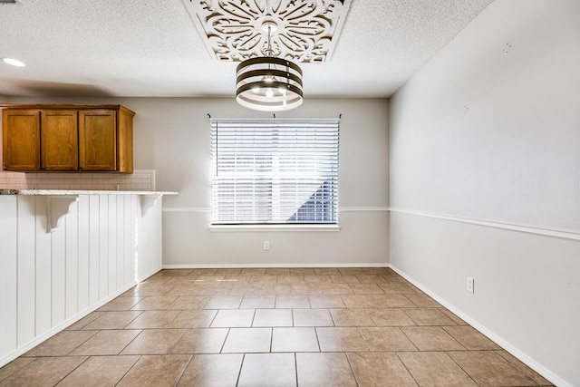 unfurnished dining area with a textured ceiling, light tile patterned flooring, and baseboards