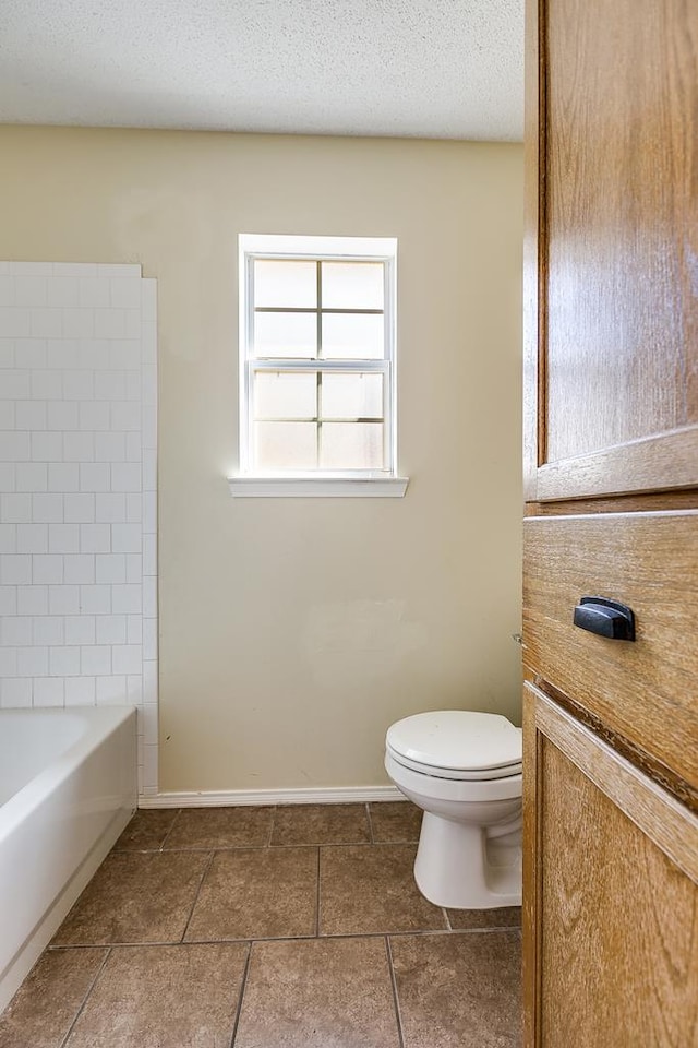 full bathroom featuring a textured ceiling, a bathing tub, toilet, baseboards, and a shower