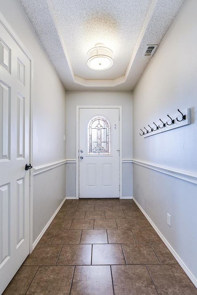 foyer with baseboards, visible vents, a tray ceiling, and a textured ceiling