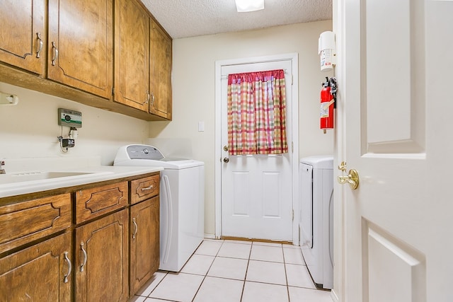 laundry area featuring sink, cabinets, light tile patterned floors, washing machine and dryer, and a textured ceiling