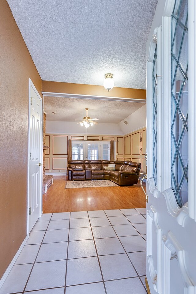 unfurnished living room featuring ceiling fan, lofted ceiling, a textured ceiling, and light tile patterned floors