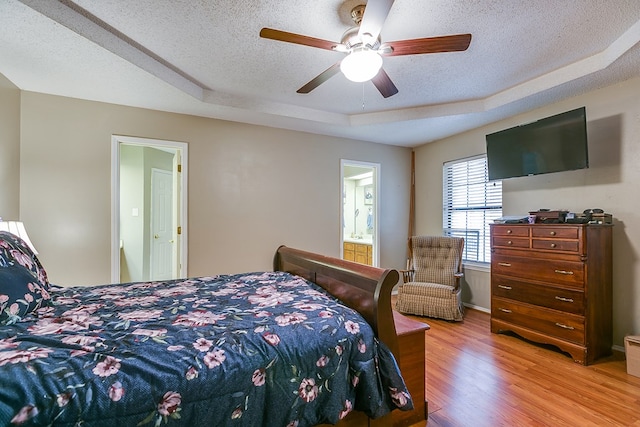 bedroom featuring a raised ceiling, light wood-type flooring, a textured ceiling, and ceiling fan