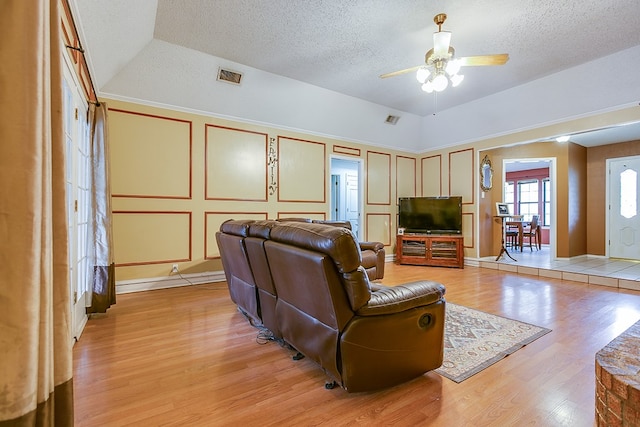 living room with a raised ceiling, ceiling fan, a textured ceiling, and light hardwood / wood-style floors