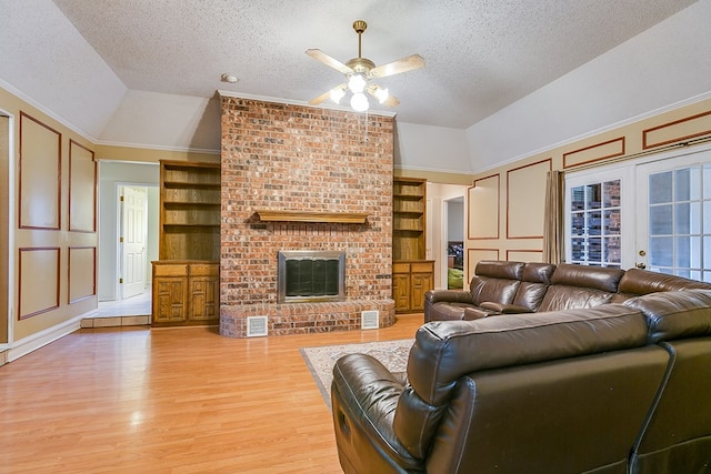 living room featuring lofted ceiling, a brick fireplace, light wood-type flooring, a textured ceiling, and built in features